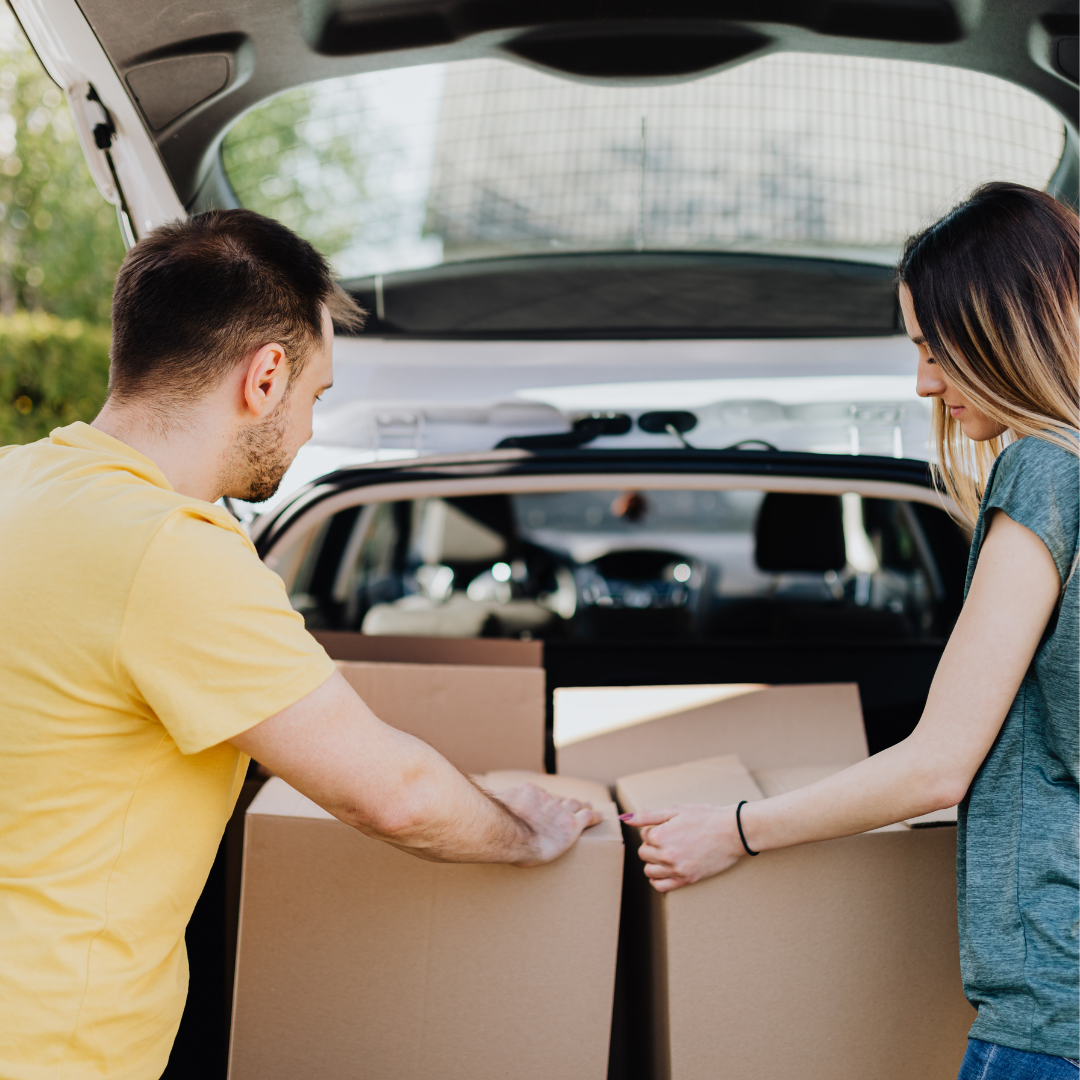 Two people moving boxes out of the trunk of a car
